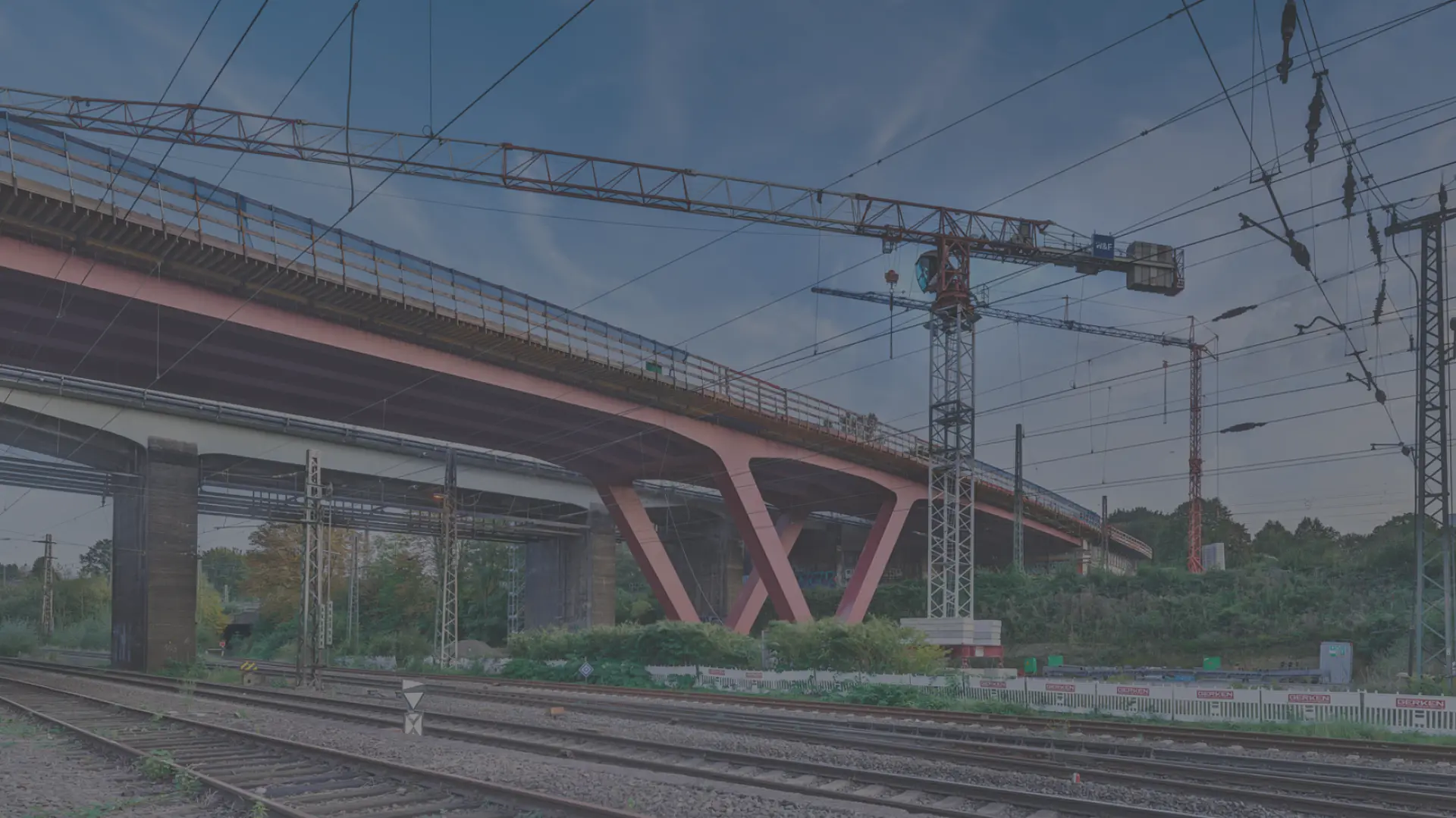 Ein Kran und eine rote Brücke im Hintergrund, im Vordergrund sind Bahngleise