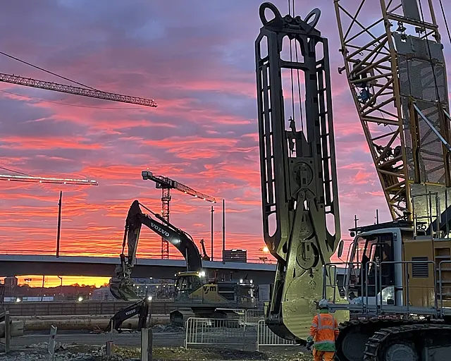 Eine Baustelle in rosa Licht getaucht, im Vordergrund ist ein Schlitzwandgreifer zu sehen
