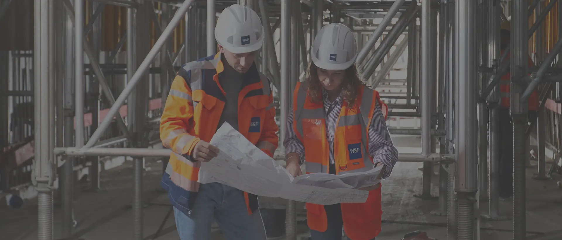 Zwei Mitarbeiter in Sicherheitskleidung auf der Baustelle schauen sich einen Plan an.