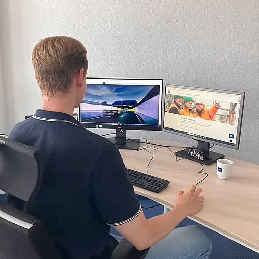 Ein Mitarbeiter sitzt am Schreibtisch vor zwei Bildschirmen.
