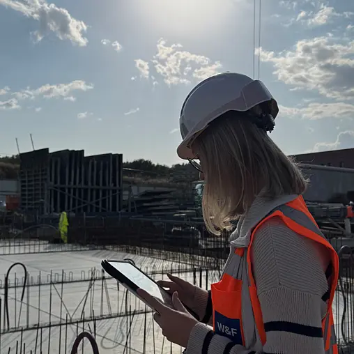 Eine Person steht mit Tablet an einer Baustelle.