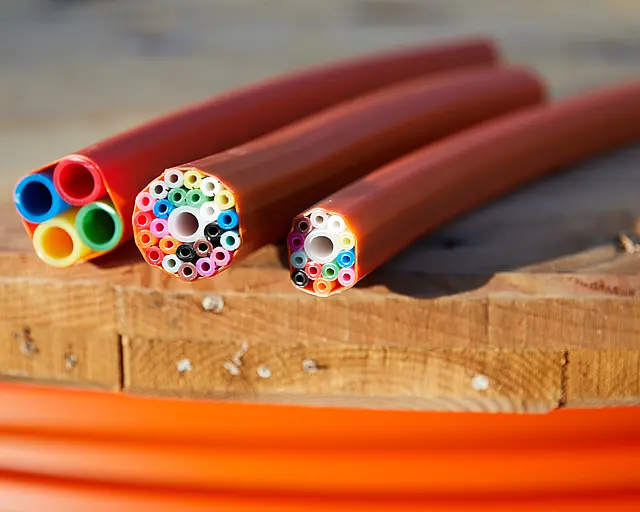 Drei Kabel für den Breitbandausbau liegen nebeneinander. Sie haben einen Querschnitt, sodass man die innenliegenden bunten Kabel erkennen kann. 