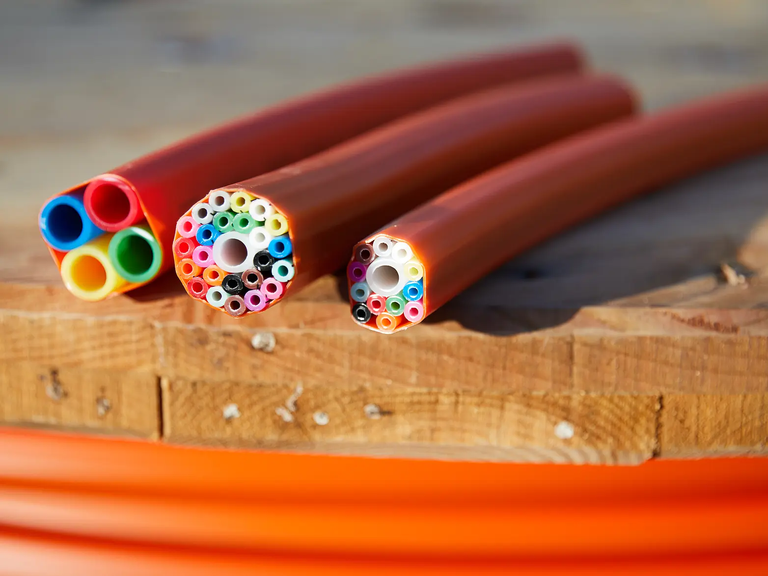 Drei Kabel für den Breitbandausbau liegen nebeneinander. Sie haben einen Querschnitt, sodass man die innenliegenden bunten Kabel erkennen kann. 