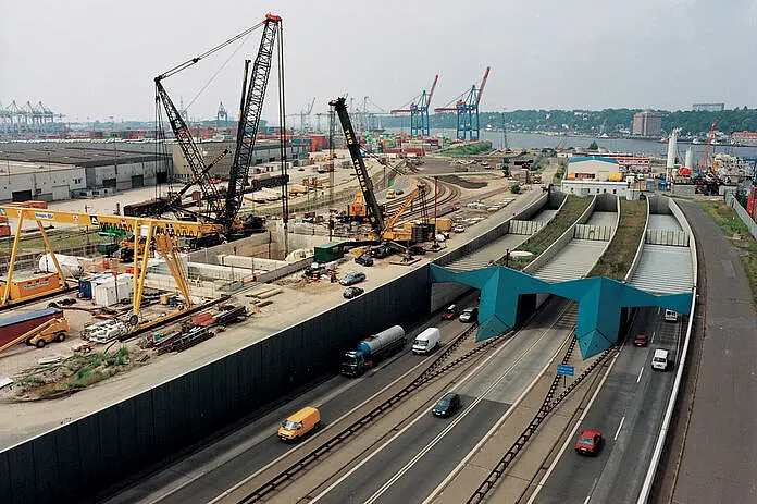 Kräne und daneben eine Autobahn mit Tunnel.