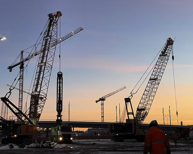 Mehrere große Maschinen und Kräne vor einem Sonnenaufgang oder Sonnenuntergang