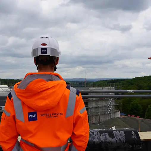 Man sieht einen Mitarbeiter von hinten der vor einer Baustelle steht. 