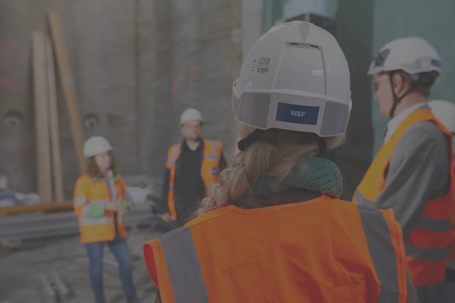Eine Frau mit Zopf und weißem Bauhelm, man sieht das blaue Logo von hinten.