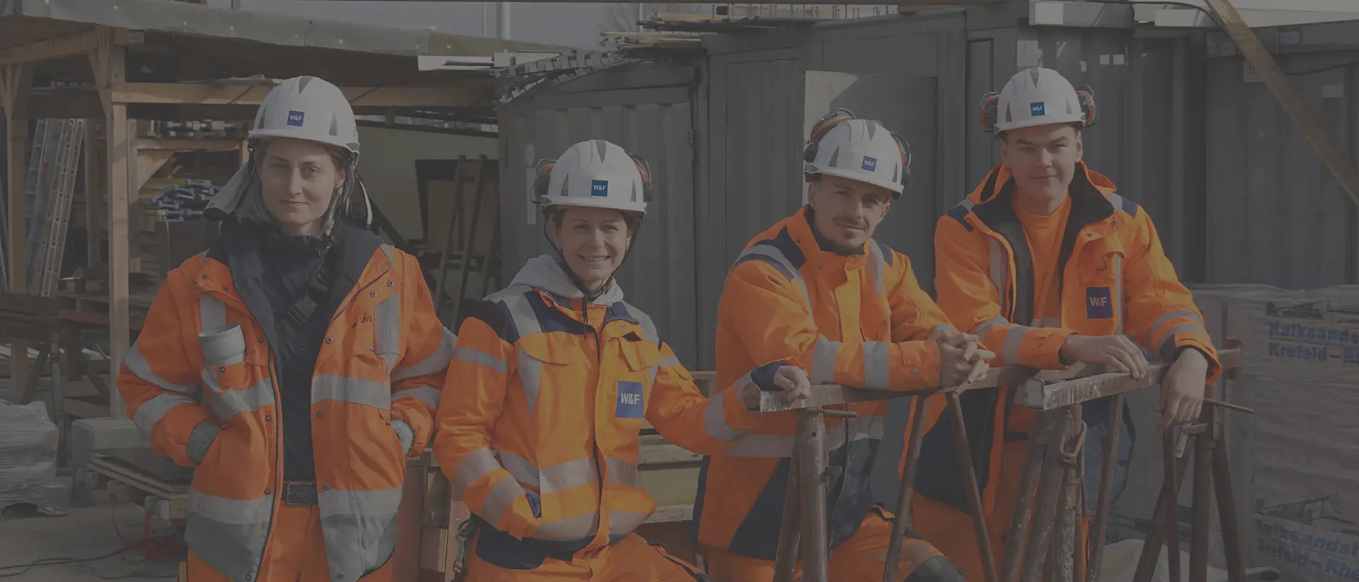 Vier Auszubildende stehen auf der Baustelle mit Sicherheitskleidung.