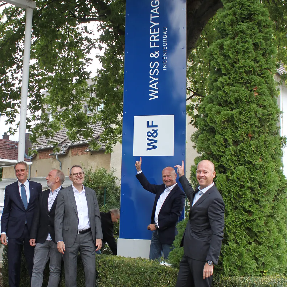 Die Vorstände von Wayss & Freytag stehen vor dem neuen blau-weißen Logo. 