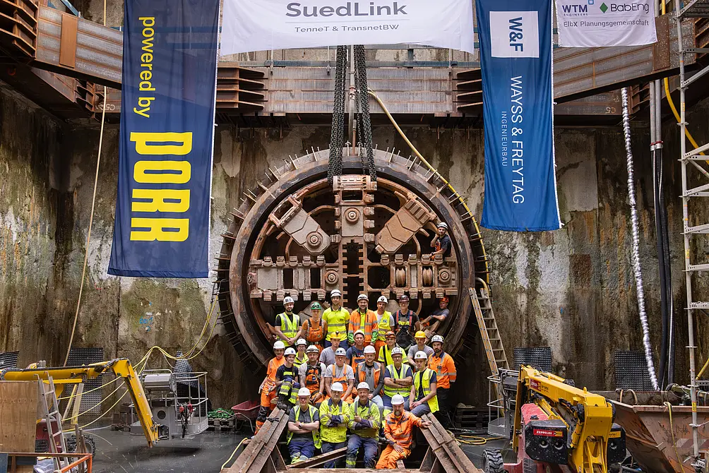 Das Tunnelbauteam vor der Tunnelbohrmaschine, an den Seiten zwei Flaggen.