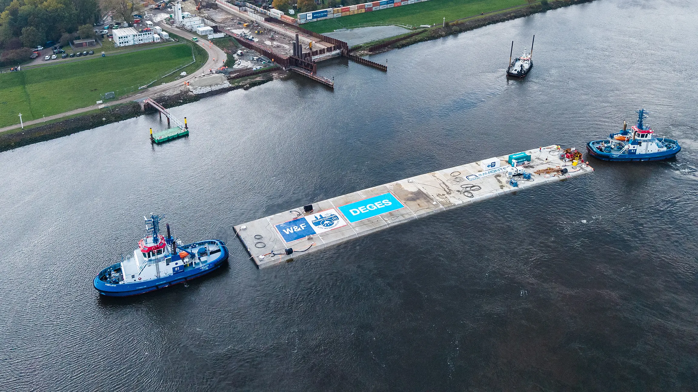 Ein Schiff zieht ein Tunnelbauteil über einen Fluss.