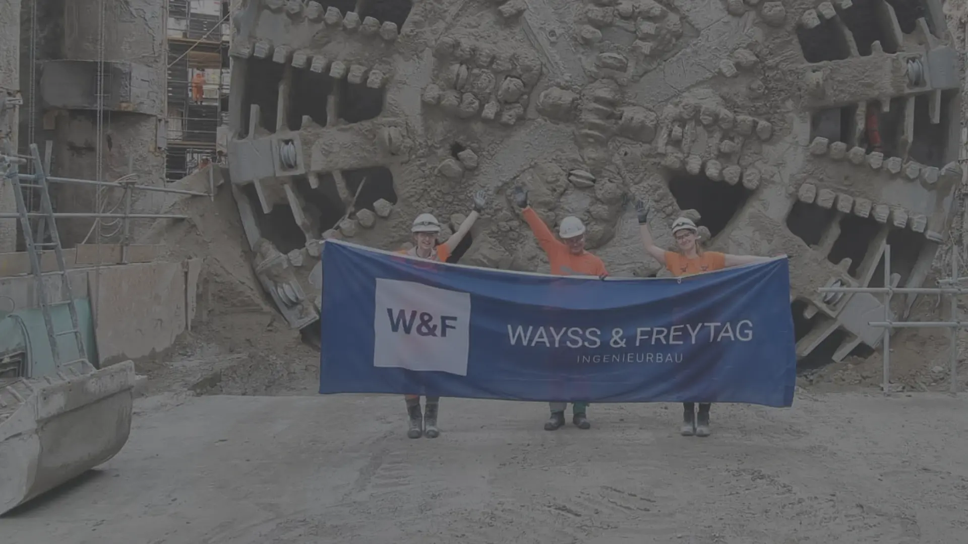 3 Mitarbeiter stehen vor einer großen Tunnelbohrmaschine und halten das Logo des Unternehmens in der Hand.